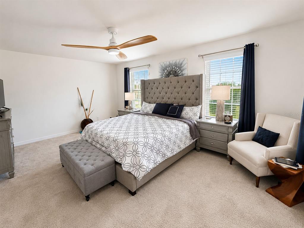 A bedroom features a tufted gray headboard, a patterned bedspread, and a ceiling fan — 1254 WISPY CYPRESS DRIVE, KISSIMMEE, FL