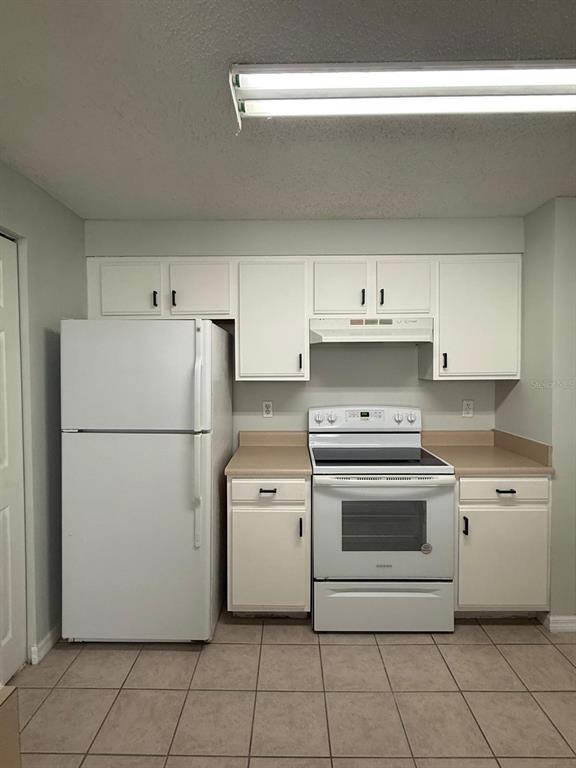 A kitchen features white cabinets, a white refrigerator, a white stove, and tiled flooring — 10831 WINDSOR WALK DRIVE UNIT 311, ORLANDO, FL