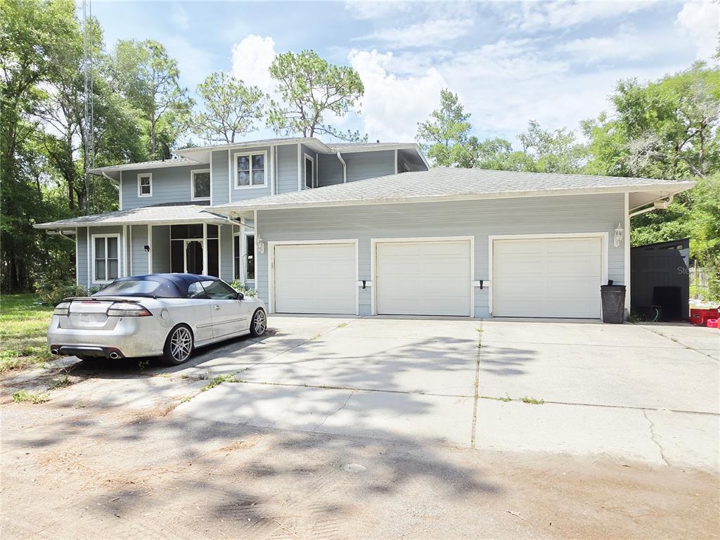 A two-story light blue house with a three-car garage and a silver convertible parked outside — 2975 E WITHLACOOCHEE TRAIL, DUNNELLON, FL