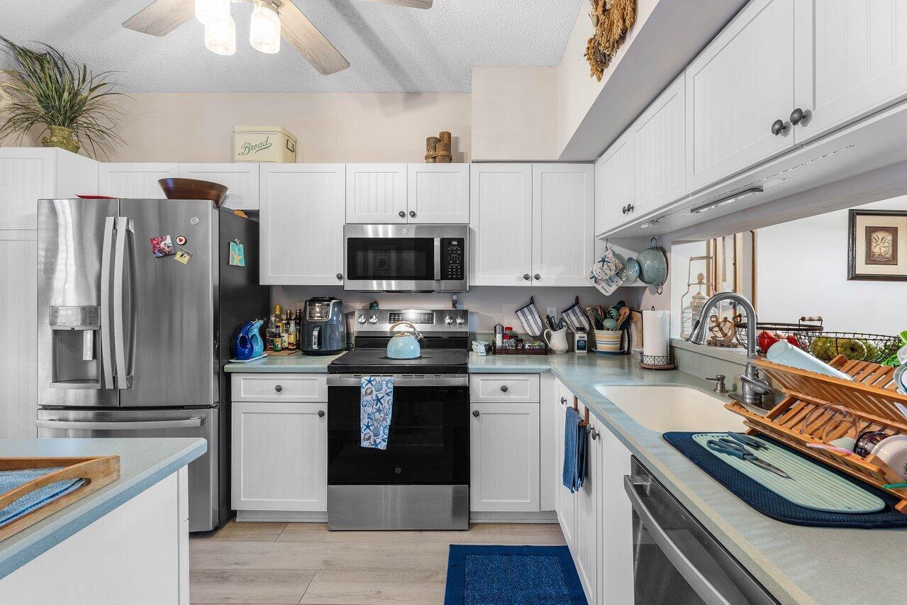 A kitchen features white cabinetry, stainless steel appliances, and light blue countertops — 1022 Kokomo Key Lane, Delray Beach FL 33483, DELRAY BEACH, FL