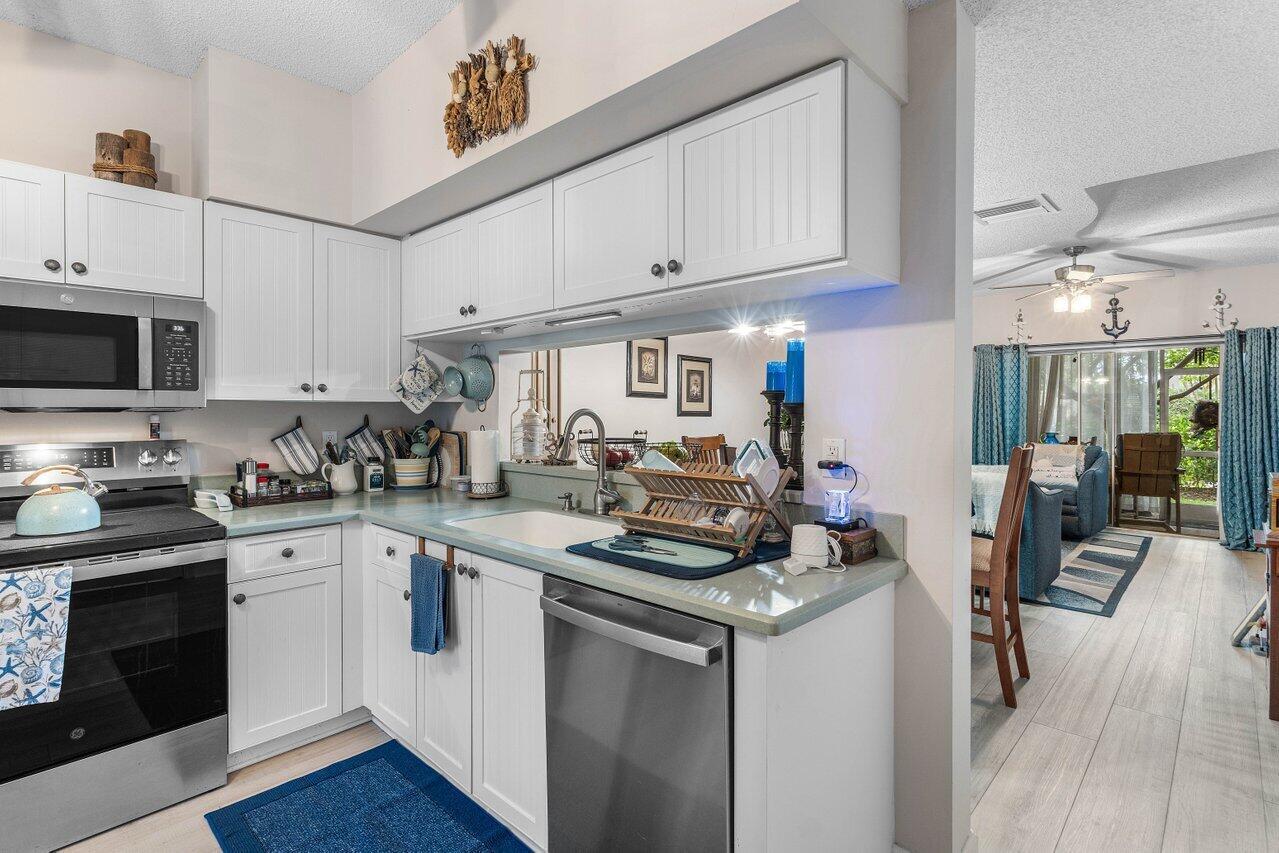 A kitchen with white cabinets, stainless steel appliances, and a view into the living area — 1022 Kokomo Key Lane, Delray Beach FL 33483, DELRAY BEACH, FL