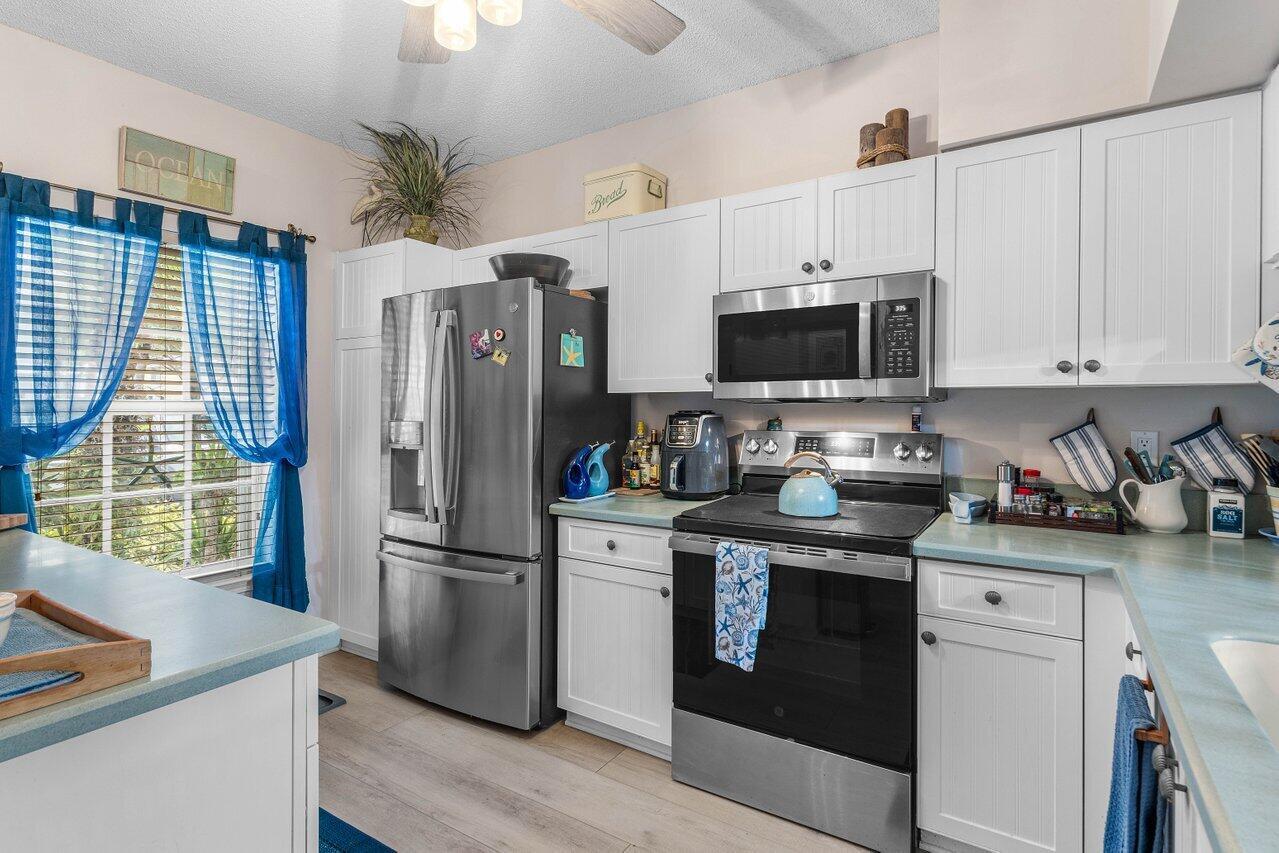 A kitchen features white cabinets, stainless steel appliances, and light blue countertops — 1022 Kokomo Key Lane, Delray Beach FL 33483, DELRAY BEACH, FL