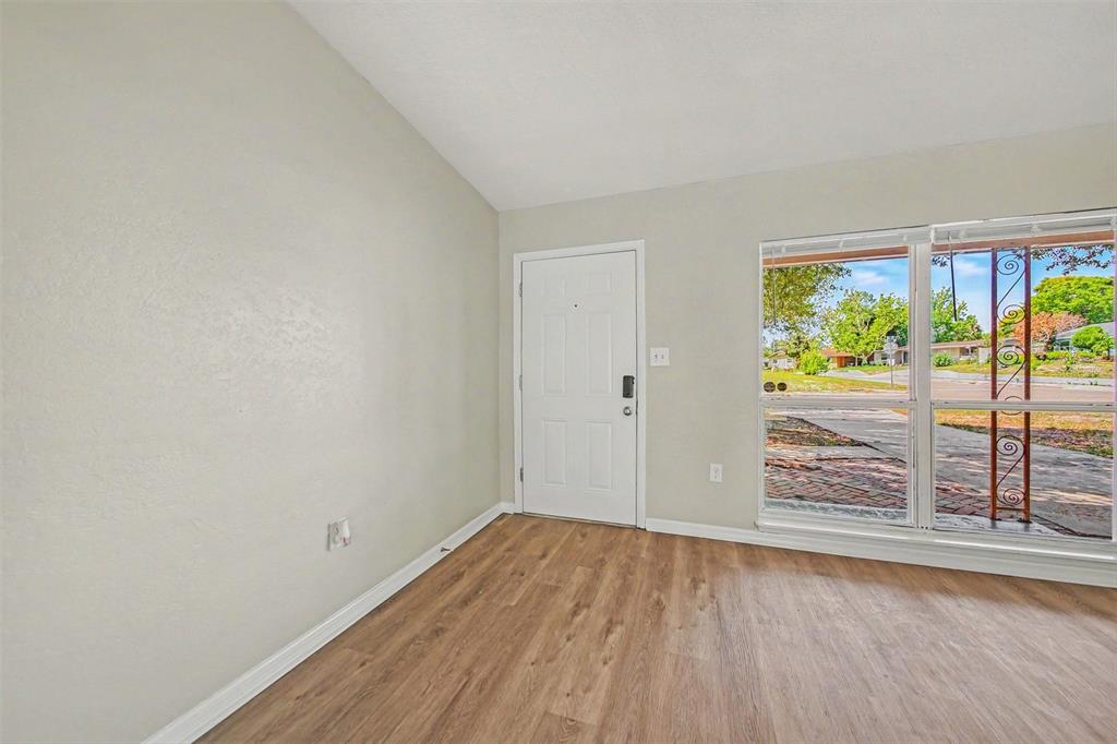 An empty room features light gray walls, wood-look flooring, a white front door, and windows — 5909 WOLF ROAD, ORLANDO, FL