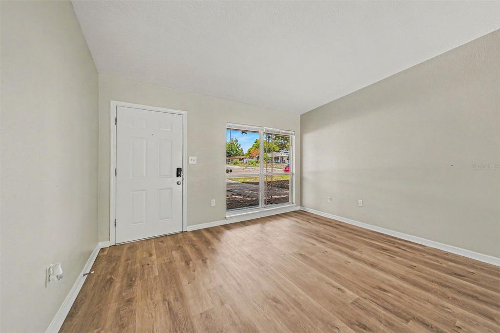 An empty room with light-colored walls, wood-look flooring, a white entry door, and a window — 5909 WOLF ROAD, ORLANDO, FL