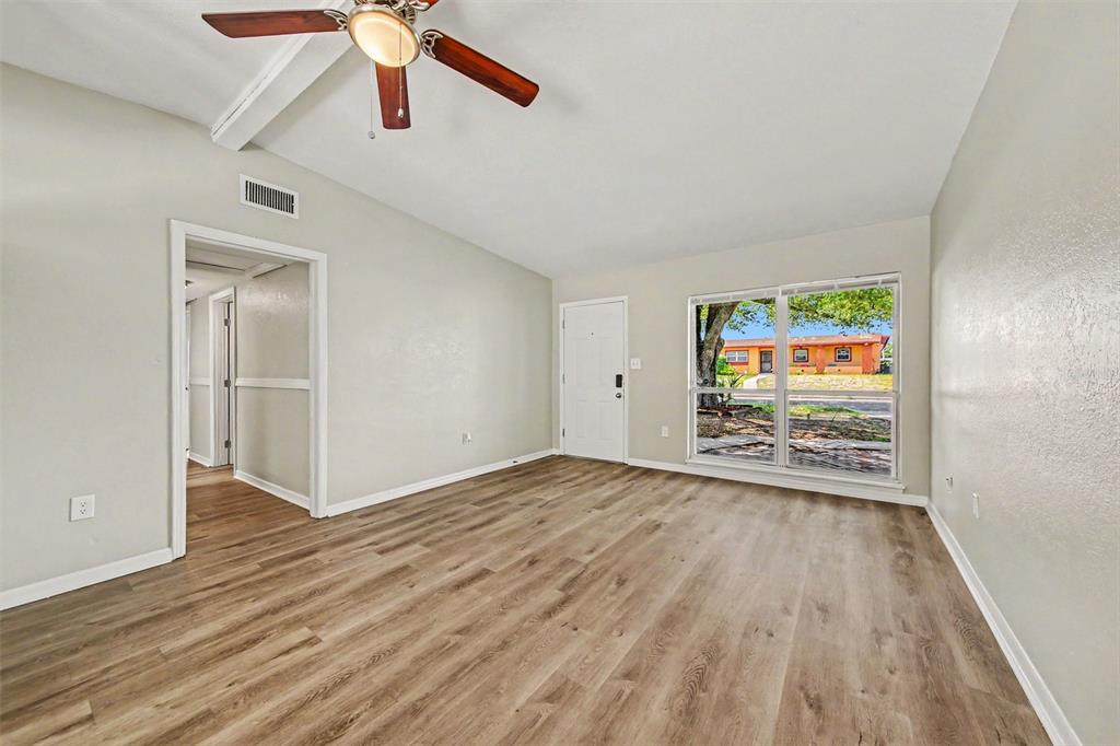 An empty living room features light-colored walls, wood-look flooring, a ceiling fan, and large windows — 5909 WOLF ROAD, ORLANDO, FL