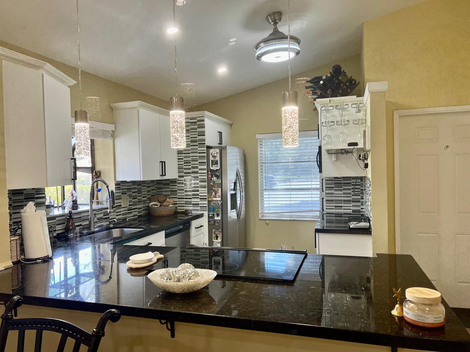 A kitchen features white cabinets, black countertops, a glass cooktop, and decorative pendant lighting — 8053 Springtree Road # 8053, Boca Raton FL 33496, BOCA RATON, FL
