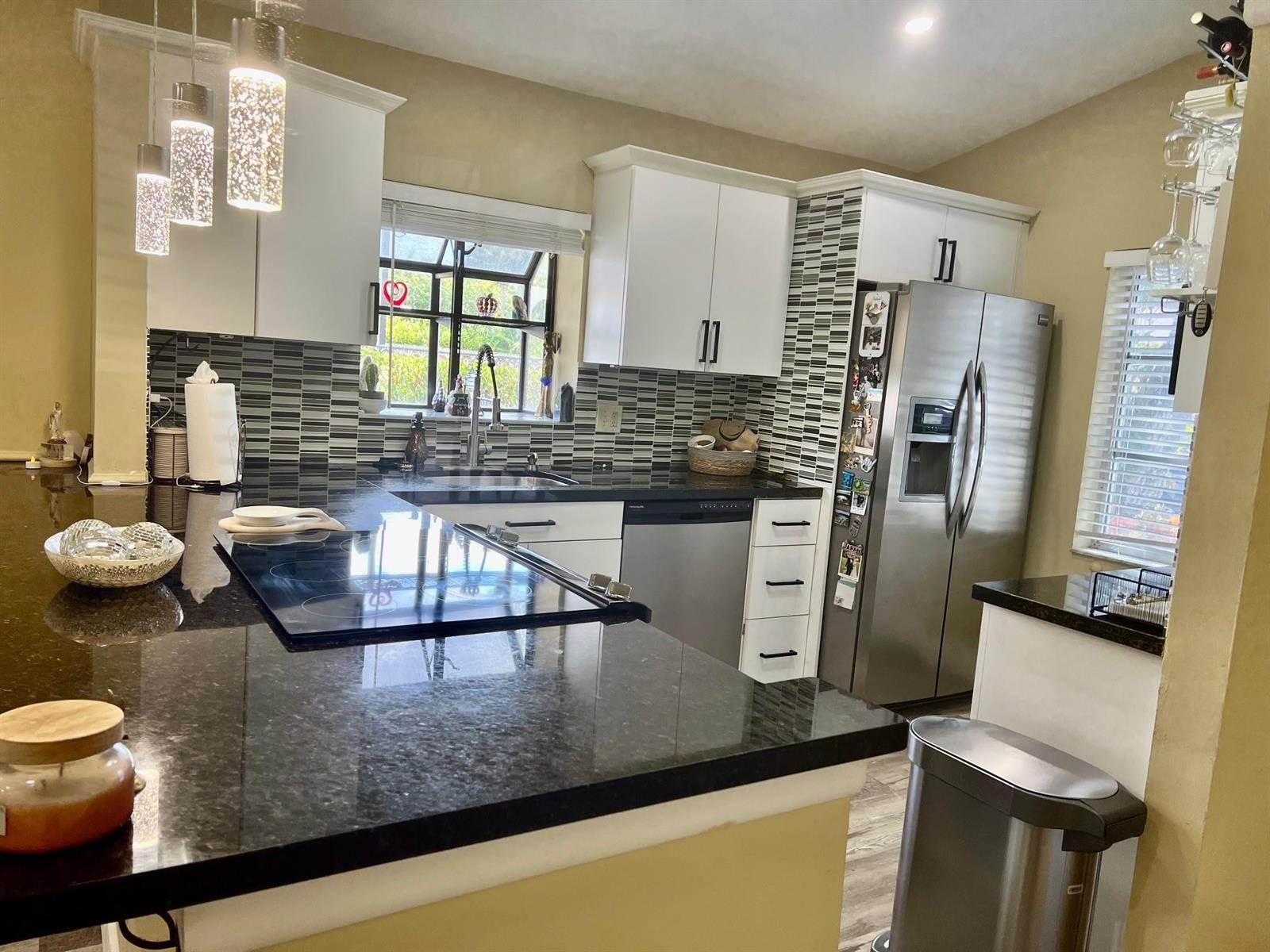 A kitchen features white cabinets, black granite countertops, stainless steel appliances, and a tiled backsplash — 8053 Springtree Road # 8053, Boca Raton FL 33496, BOCA RATON, FL