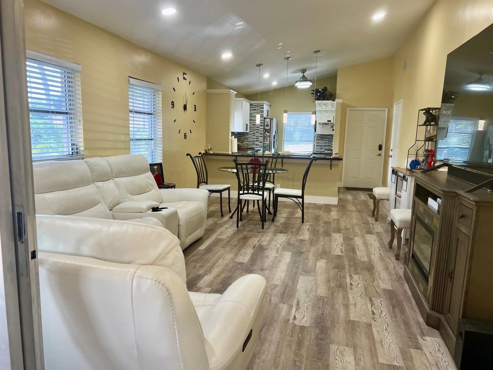 An open-concept living room and kitchen featuring white leather seating, wood-look flooring, and a dining area — 8053 Springtree Road # 8053, Boca Raton FL 33496, BOCA RATON, FL