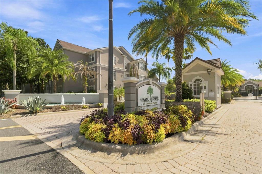 The entrance to an apartment complex features a stone sign, landscaping, and a gated driveway — 3379 S KIRKMAN ROAD UNIT 1027, ORLANDO, FL
