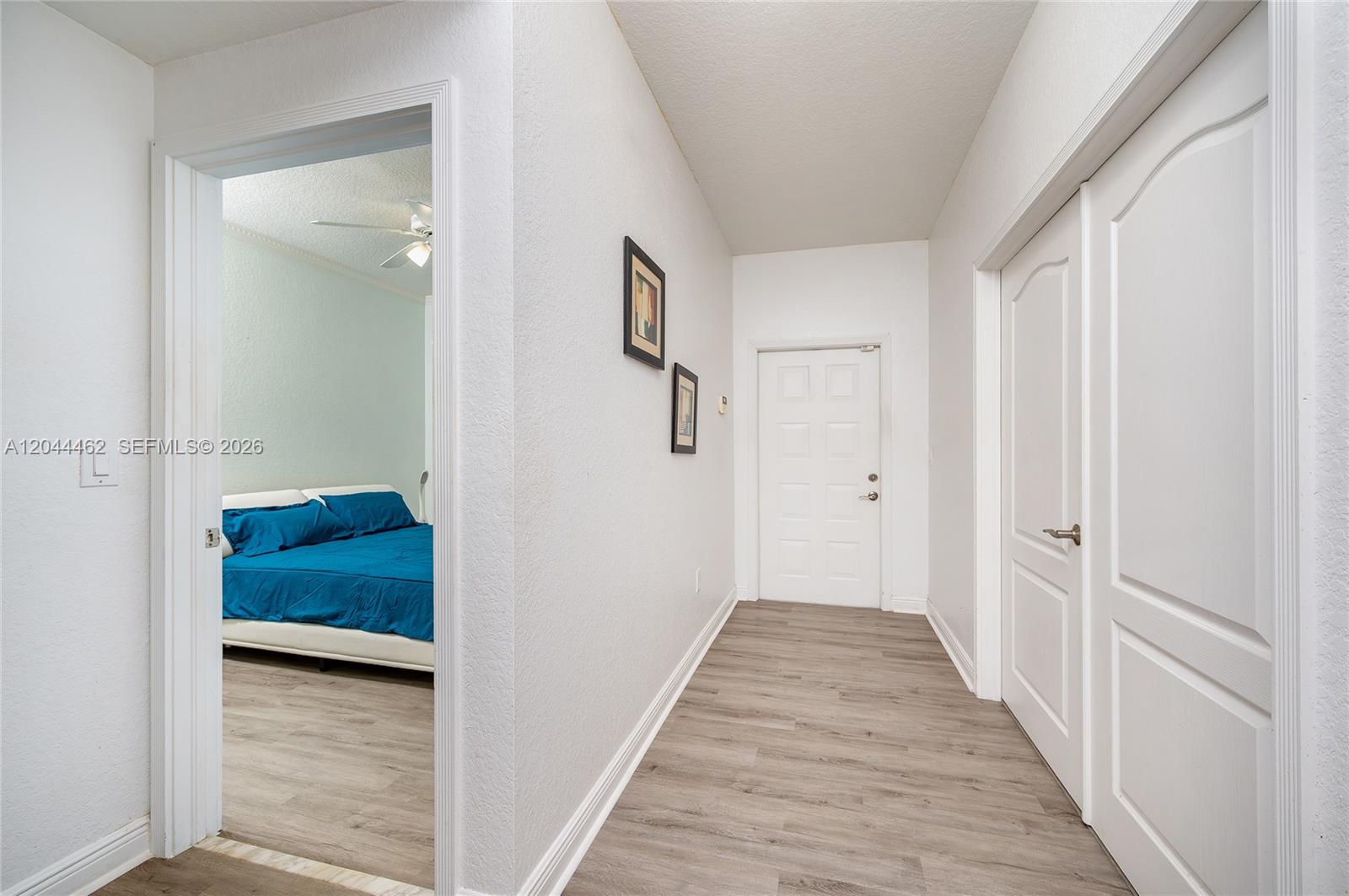 A hallway with light wood-look flooring leads to a white door, with a bedroom visible — 10700 NW 66th St # 204, Doral FL 33178, DORAL, FL