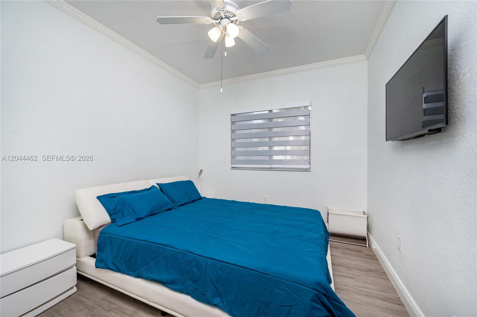 A bedroom features a white bed with blue bedding, a ceiling fan, and a wall-mounted television — 10700 NW 66th St # 204, Doral FL 33178, DORAL, FL