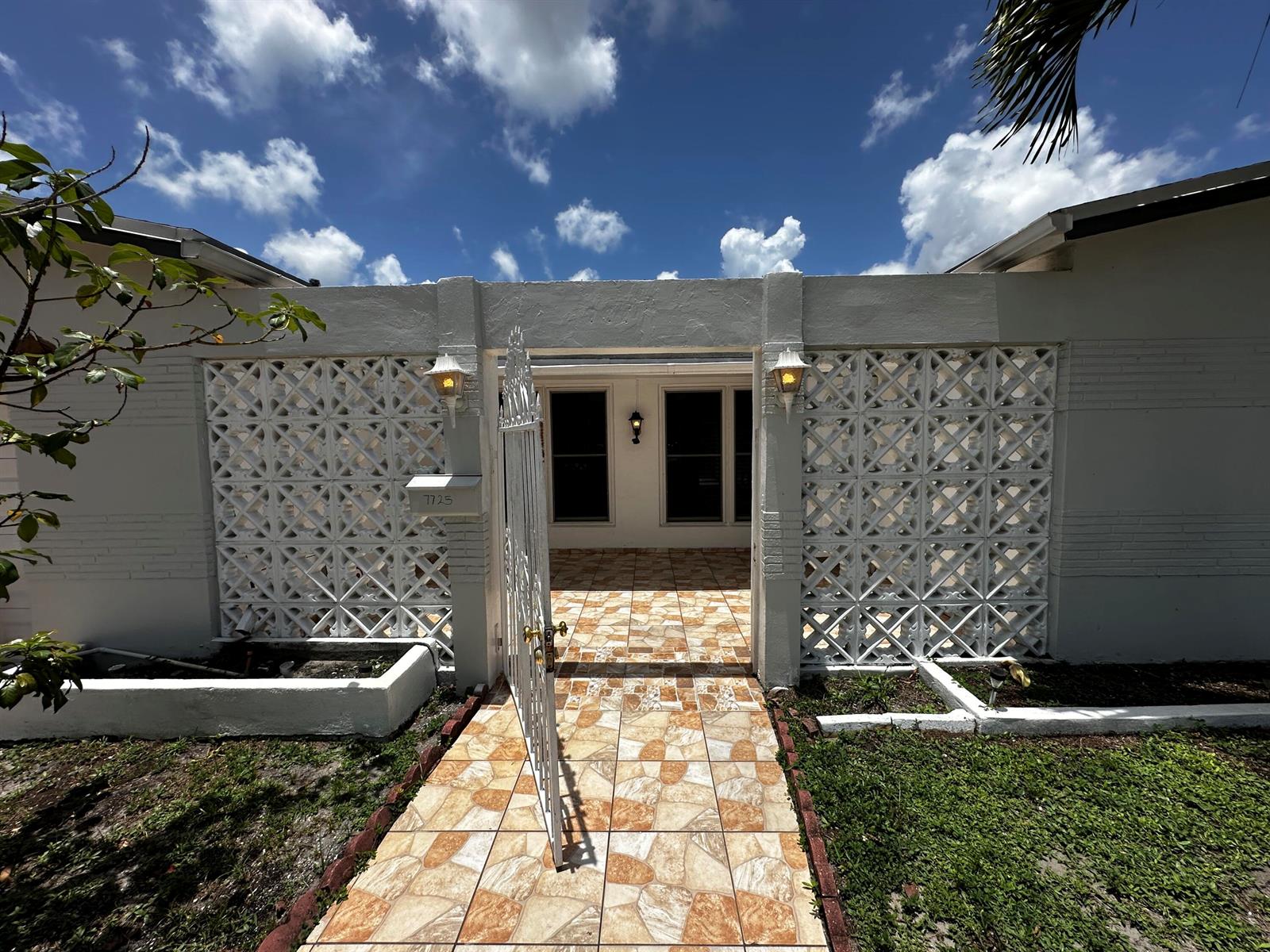 A white house exterior features a decorative breeze block wall, a tiled walkway, and gate — 7725 Grandview Boulevard # 7725, Miramar FL 33023, MIRAMAR, FL