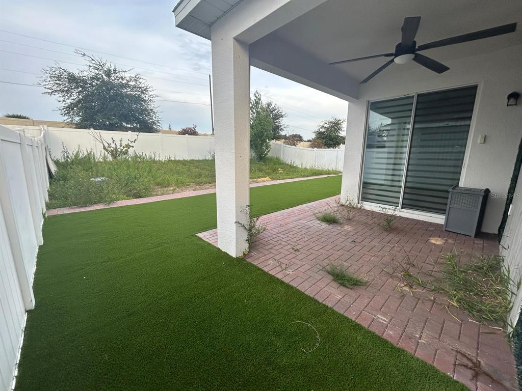A covered patio with a ceiling fan overlooks a backyard with artificial turf and pavers — 1229 HENDON LOOP, DAVENPORT, FL