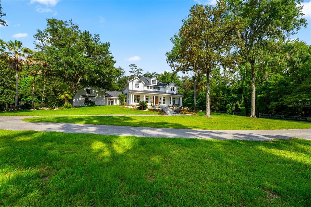 A white two-story house with a wrap-around porch sits on a grassy lot with trees — 9809 NW 59TH TERRACE, GAINESVILLE, FL