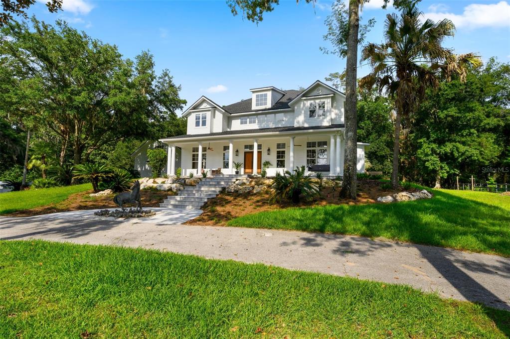 A two-story white farmhouse with a large front porch and stone steps sits on grass — 9809 NW 59TH TERRACE, GAINESVILLE, FL