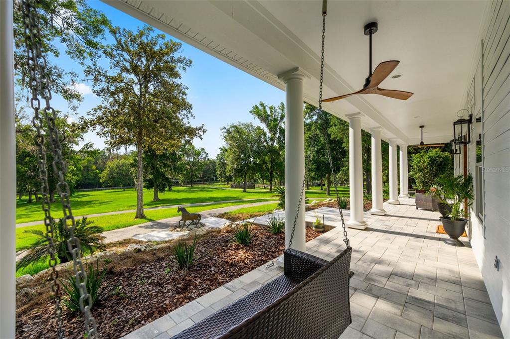 A covered porch with a hanging swing, ceiling fans, and columns overlooks a grassy yard — 9809 NW 59TH TERRACE, GAINESVILLE, FL