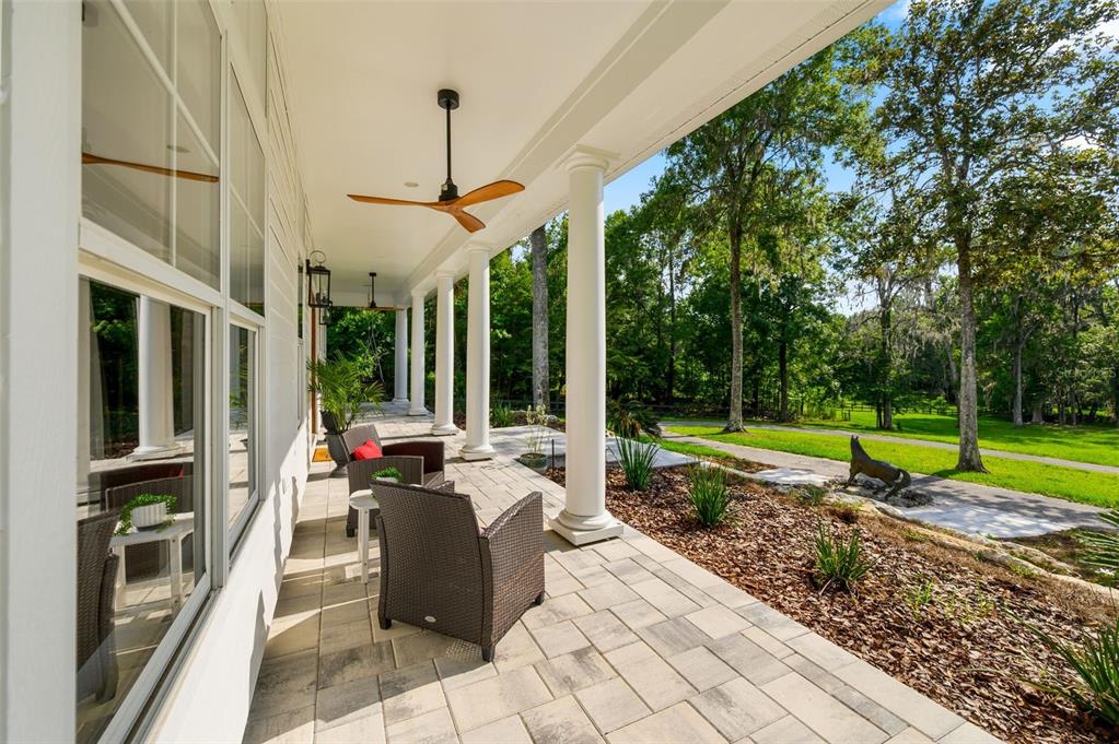 A covered patio with white columns, wicker furniture, and a ceiling fan overlooks a yard — 9809 NW 59TH TERRACE, GAINESVILLE, FL