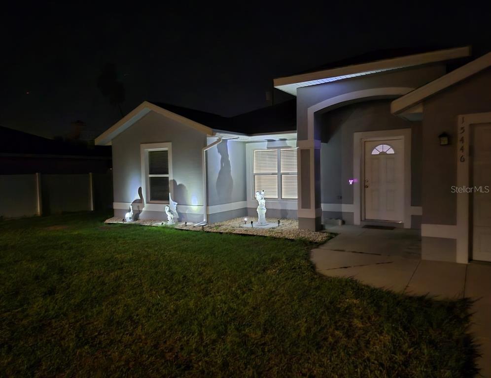 A night view of a single-story house exterior with illuminated landscaping and a front entrance — 15446 SW 23RD COURT ROAD, OCALA, FL