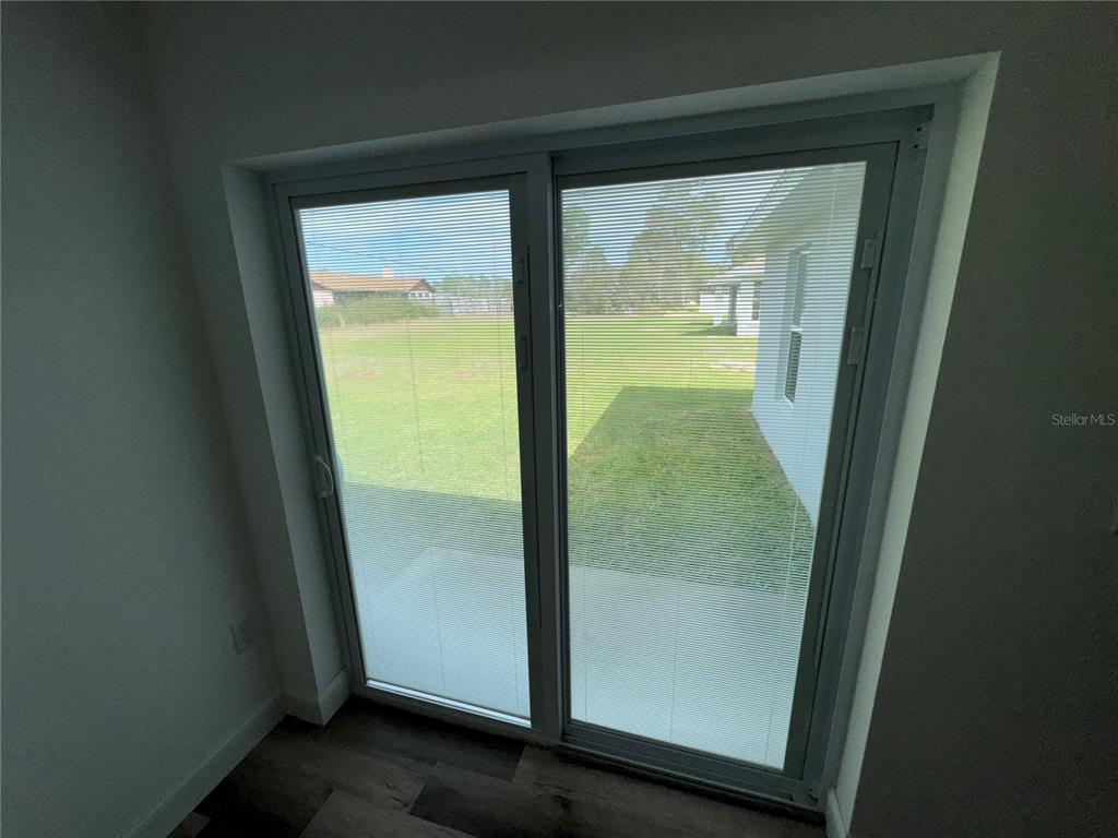 A sliding glass door with integrated blinds looks out onto a grassy backyard — 15446 SW 23RD COURT ROAD, OCALA, FL