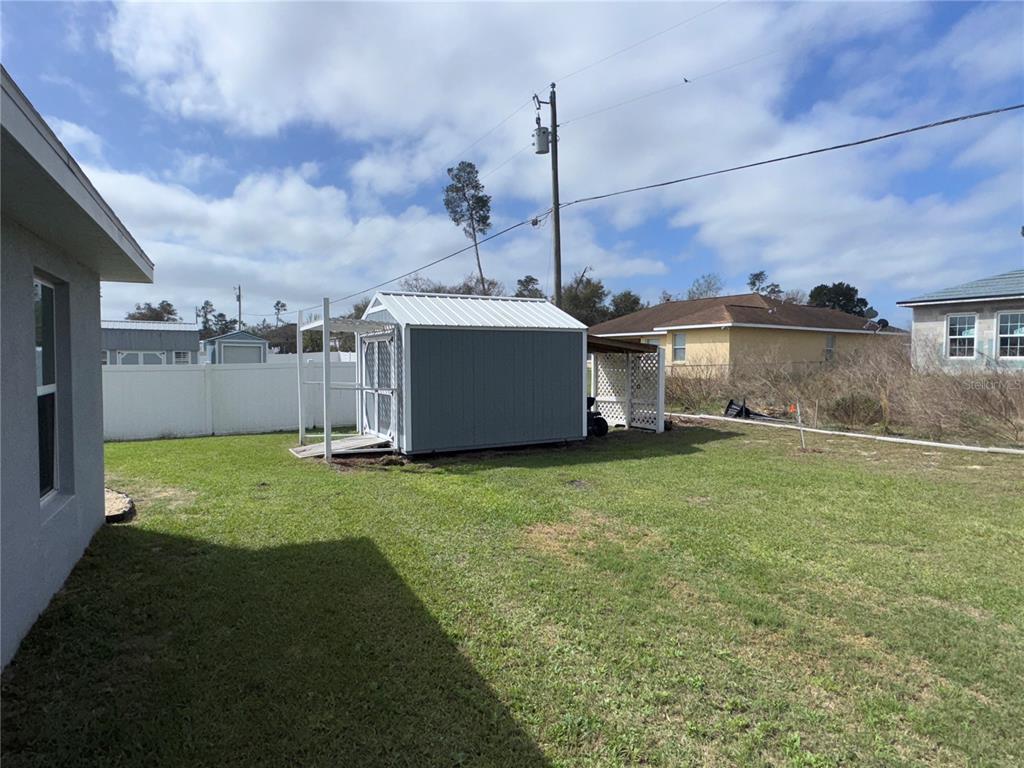 A backyard features a gray shed with a metal roof and a white fence — 15446 SW 23RD COURT ROAD, OCALA, FL