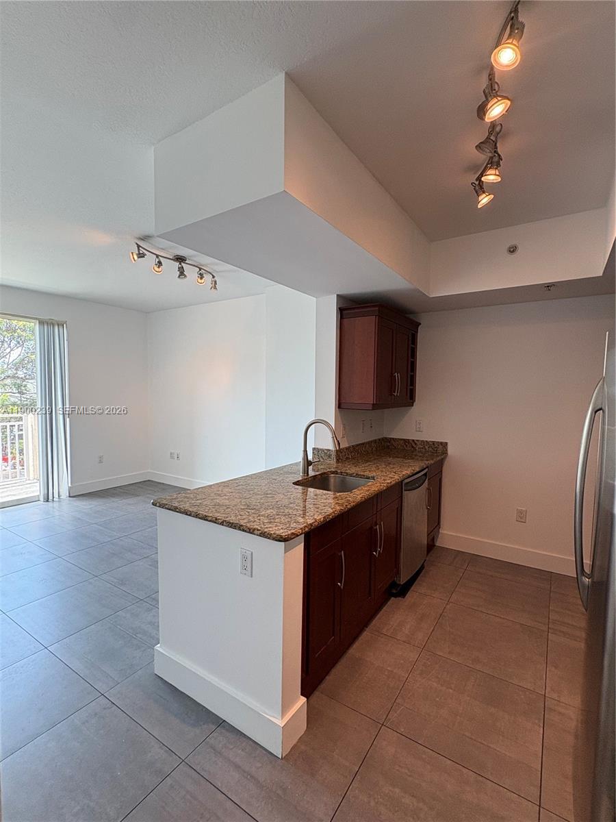 A kitchen with granite countertops and dark wood cabinets overlooks an adjacent living area — 7275 SW 90th Way # 205, Miami FL 33156, MIAMI, FL