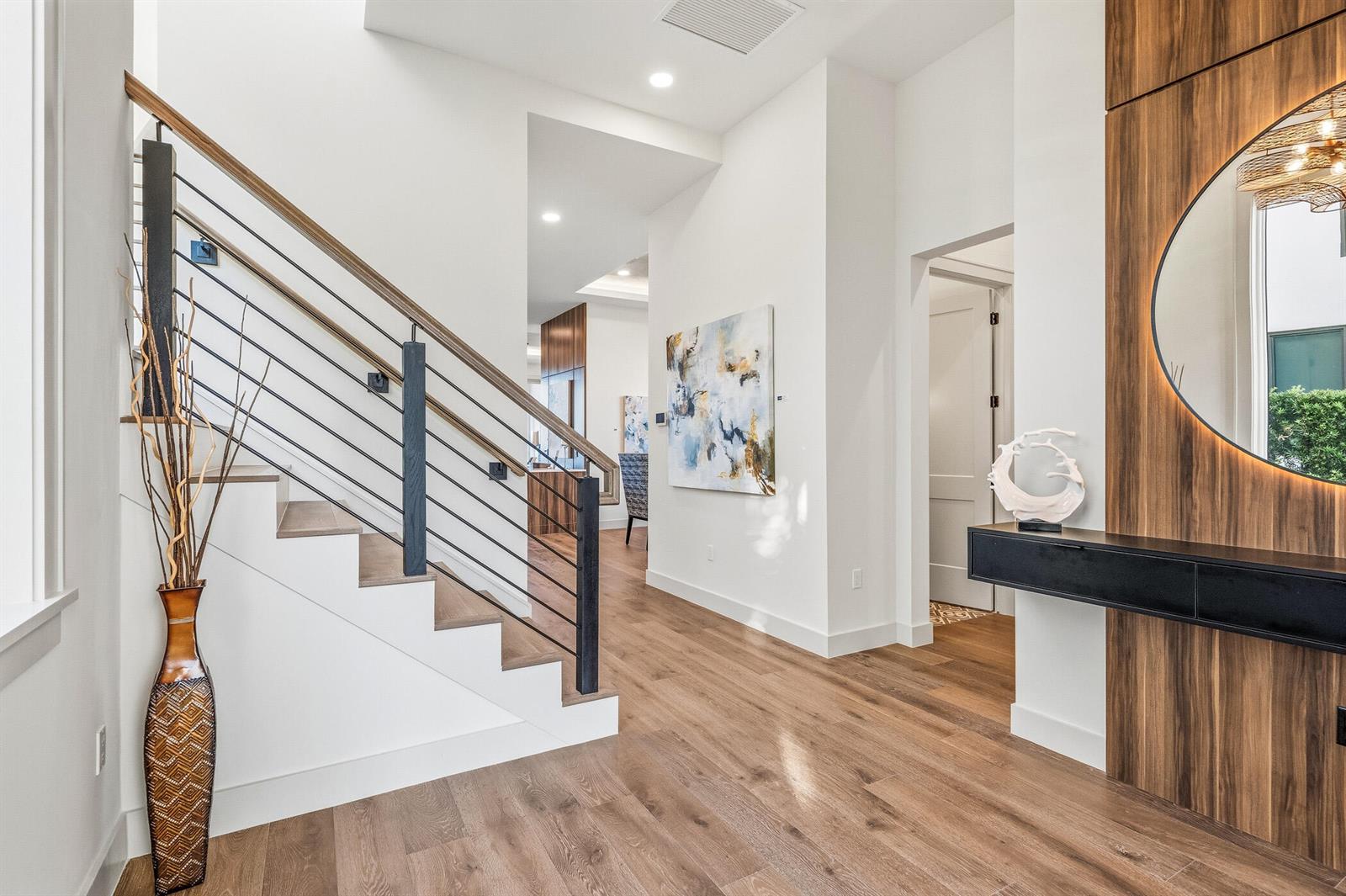 A modern entryway features a wooden staircase with metal railings, wood flooring, and a round mirror — 4842 S Harbor Drive, Vero Beach FL 32967, VERO BEACH, FL