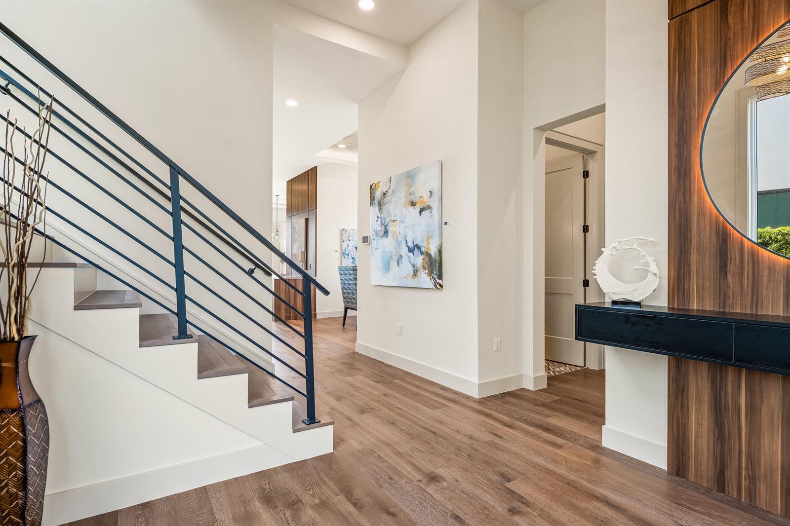 A modern entryway features a staircase with dark railings, wood flooring, and a circular mirror — 4842 S Harbor Drive, Vero Beach FL 32967, VERO BEACH, FL