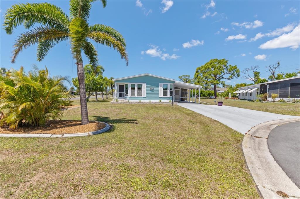 A light blue manufactured home features a palm tree, a driveway, and a grassy yard — 3308 GOLDFINCH, ENGLEWOOD, FL