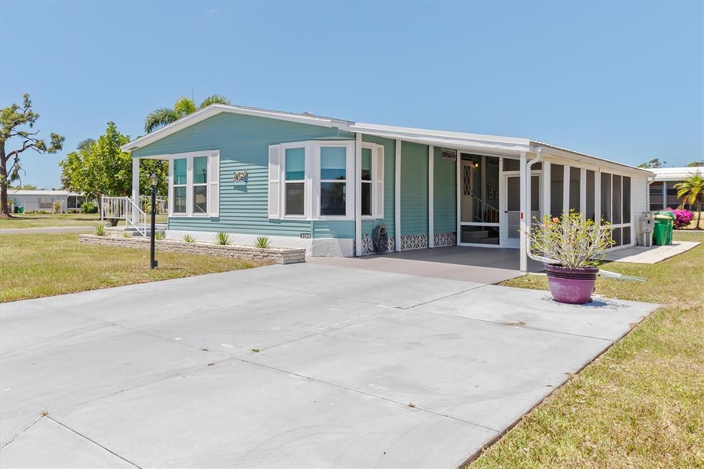 A light blue manufactured home features a concrete driveway, a screened porch, and bay windows — 3308 GOLDFINCH, ENGLEWOOD, FL