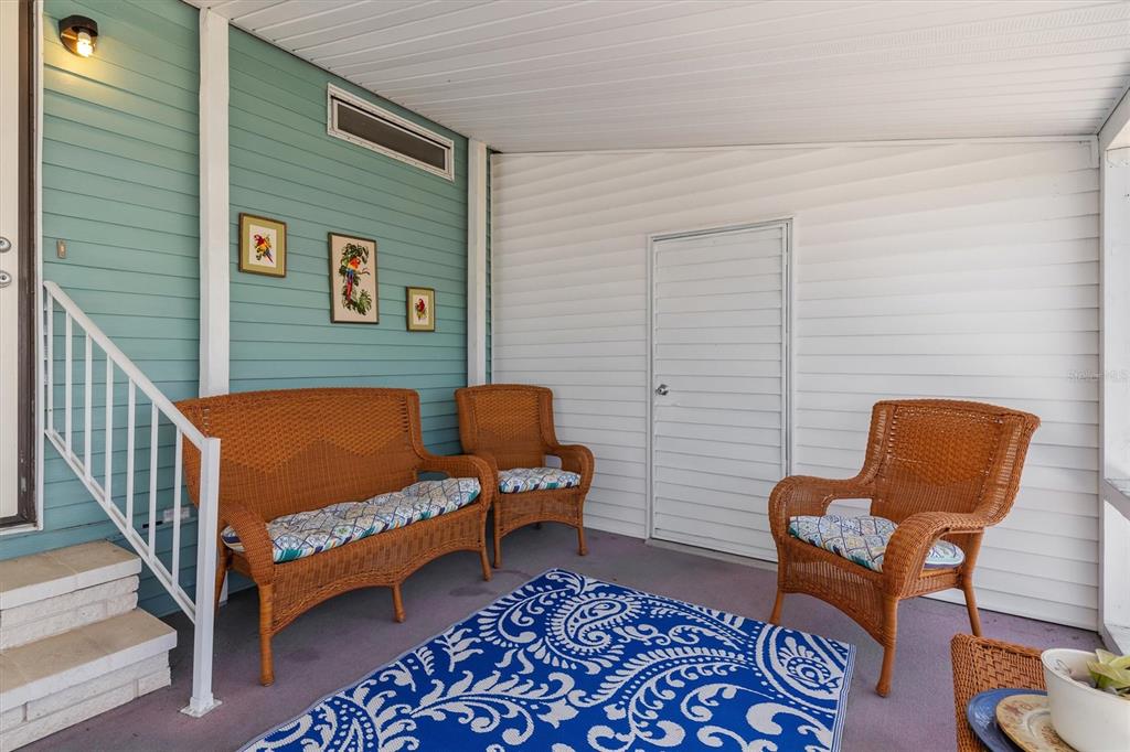 A covered porch features wicker furniture, a blue patterned rug, and teal and white siding — 3308 GOLDFINCH, ENGLEWOOD, FL