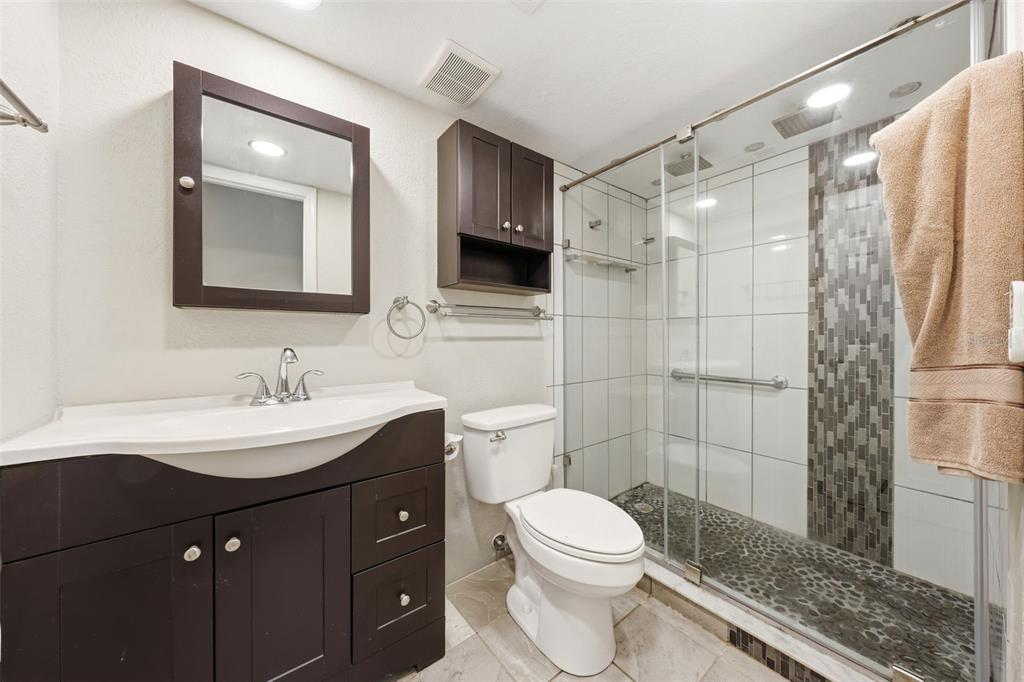 A bathroom features a dark wood vanity, a white toilet, and a glass-enclosed walk-in shower — 100 E OAK TERRACE DRIVE UNIT B2, LEESBURG, FL