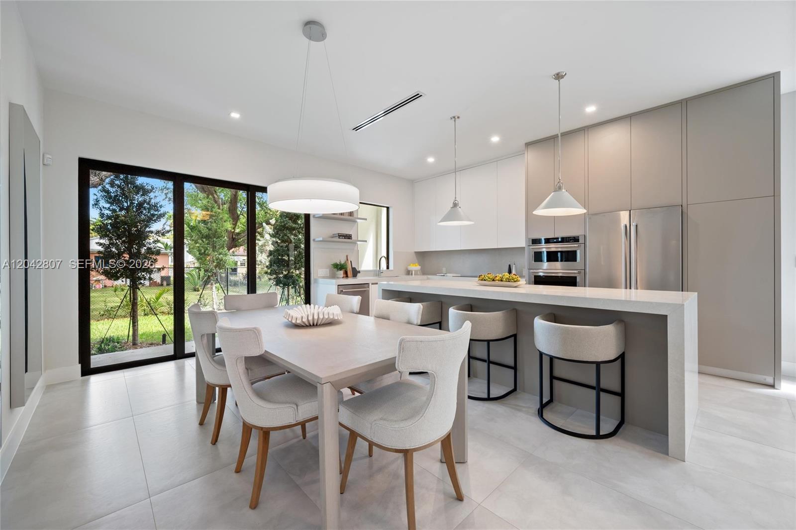 A modern kitchen and dining area features a large island, pendant lighting, and glass doors — 2747 SW 23rd Ter, Miami FL 33145, MIAMI, FL