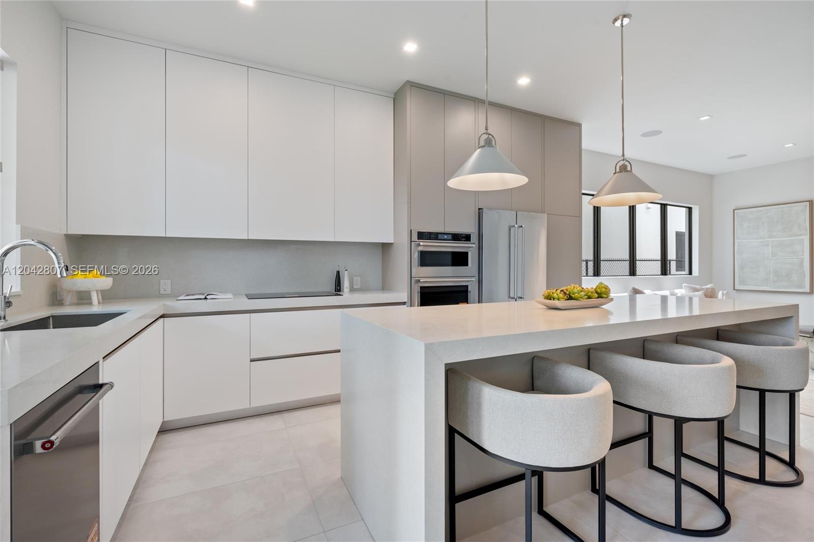 A modern kitchen features white cabinetry, a large quartz island, and three upholstered bar stools — 2747 SW 23rd Ter, Miami FL 33145, MIAMI, FL