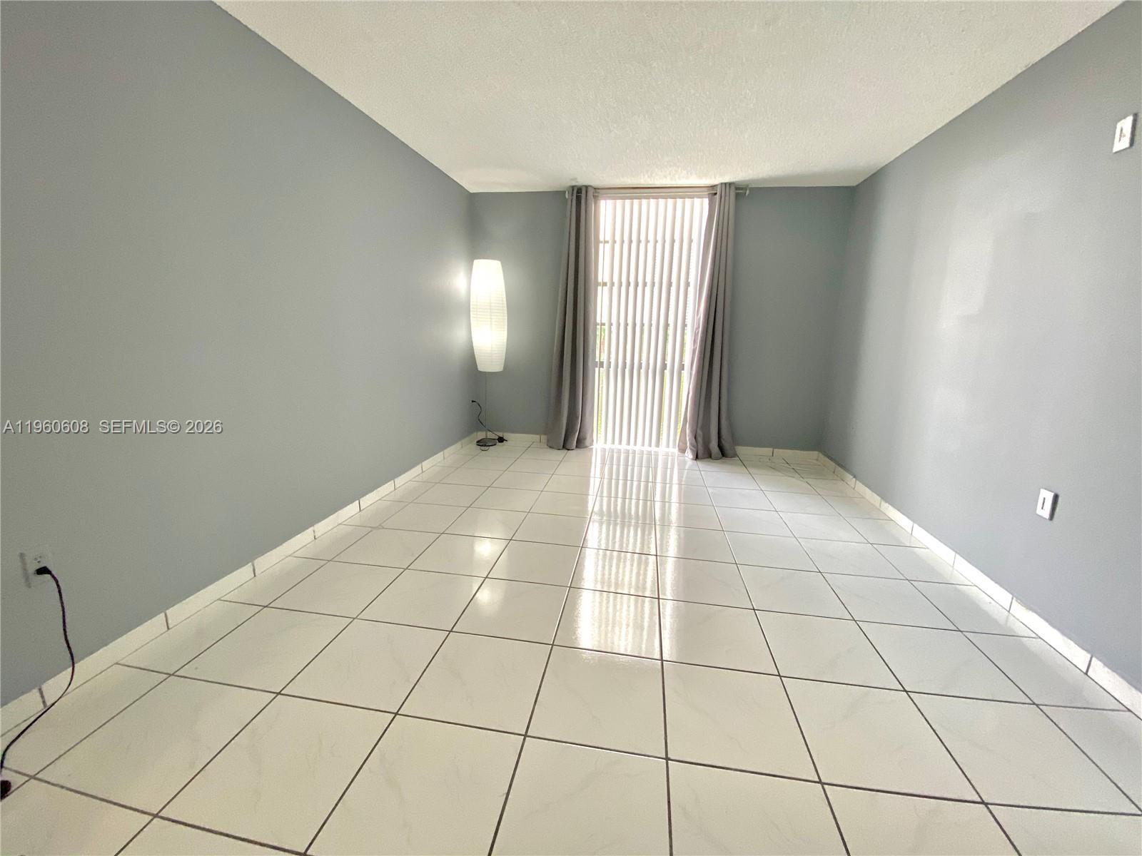 An empty room features light gray walls, white tiled floors, and a sliding glass door — 16950 DIXIE # A536, North Miami Beach FL 33160, NORTH MIAMI BEACH, FL