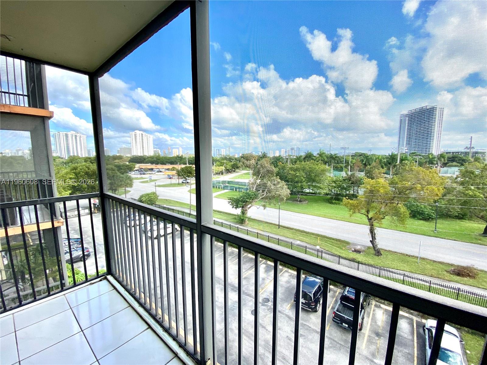 A screened-in balcony overlooks a parking lot, a grassy field, and distant city buildings — 16950 DIXIE # A536, North Miami Beach FL 33160, NORTH MIAMI BEACH, FL