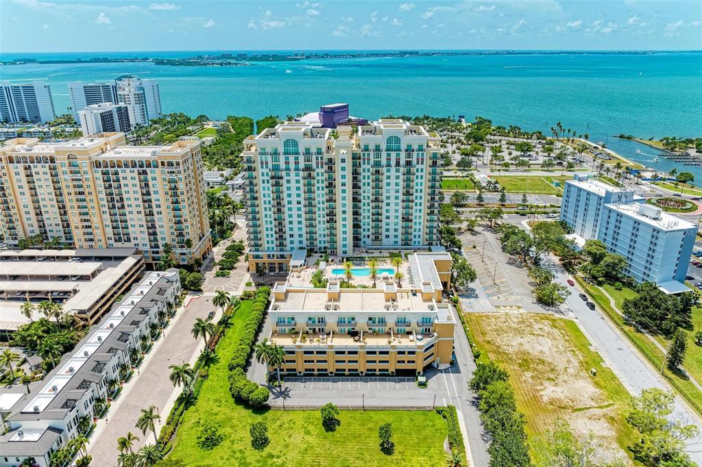 An aerial view shows high-rise apartment buildings, a swimming pool, and a nearby bay — 800 N TAMIAMI TRAIL UNIT 212, SARASOTA, FL