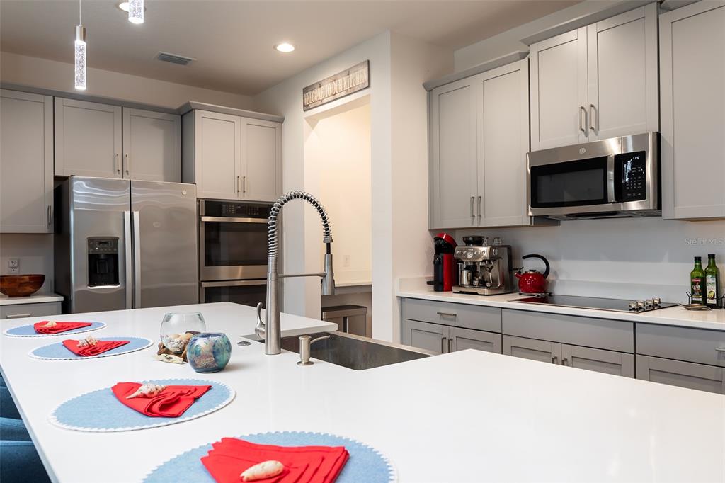 A modern kitchen features gray cabinets, stainless steel appliances, and a large white island — 5012 BESSIE COURT, ST CLOUD, FL