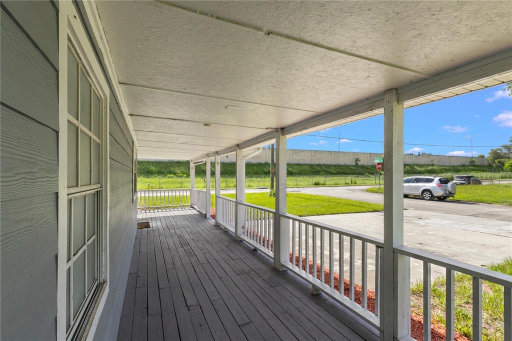 A covered wooden porch with white railings overlooks a grassy area and a nearby street — 320 E ALTHEA AVENUE, TAMPA, FL