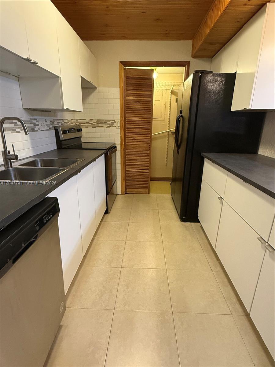 A galley kitchen features white cabinets, dark countertops, stainless steel appliances, and a tiled floor — 120 Lakeview Dr # 114, Weston FL 33326, WESTON, FL