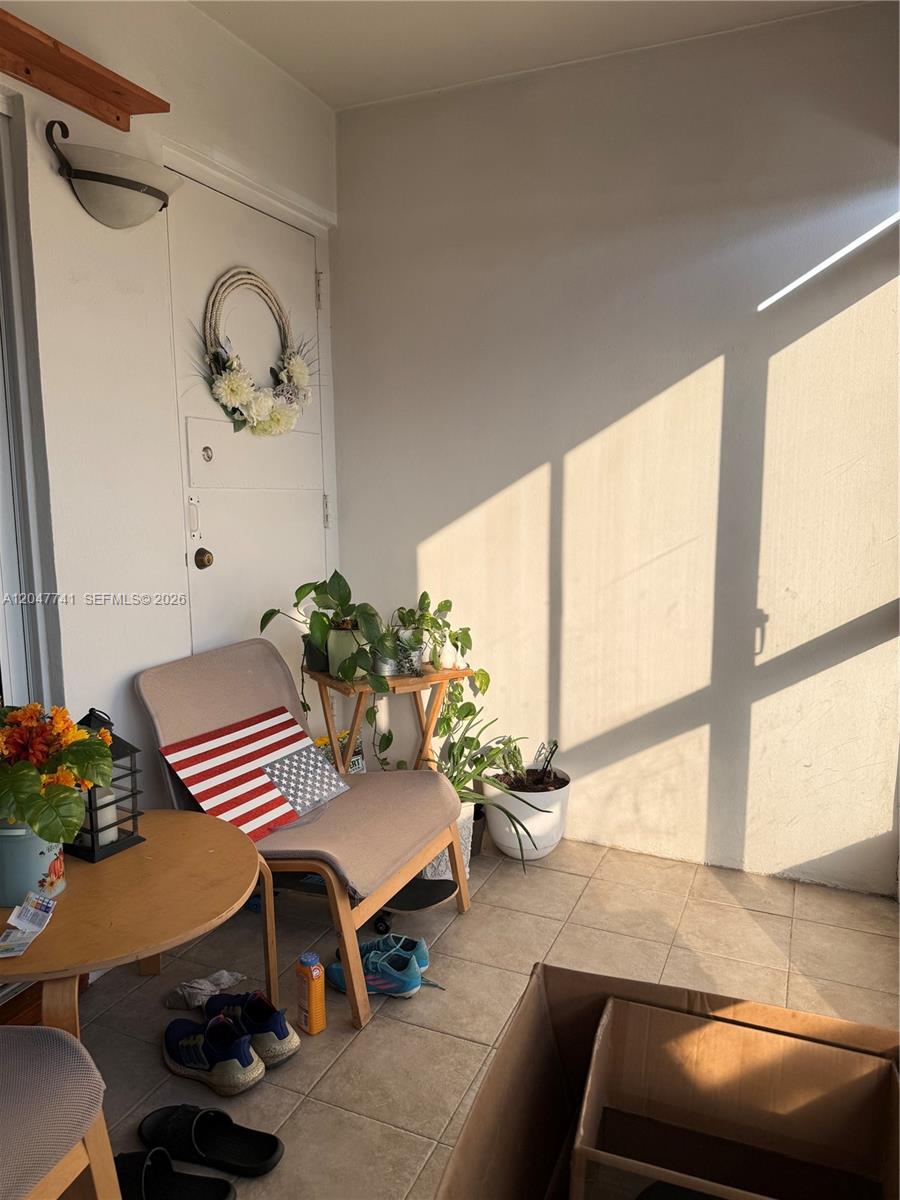 A sunlit balcony features a chair, small tables, potted plants, and a door with a wreath — 120 Lakeview Dr # 114, Weston FL 33326, WESTON, FL