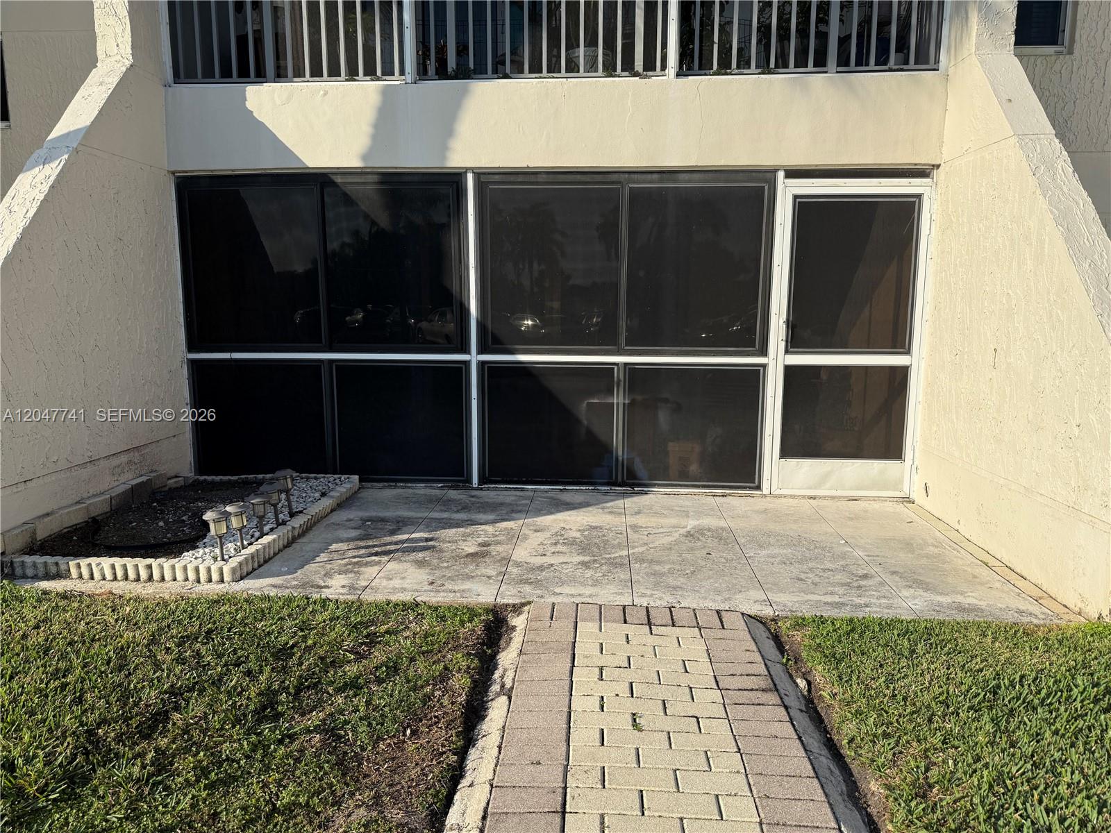 A ground-level patio features a paved walkway, a small garden bed, and screened enclosure doors — 120 Lakeview Dr # 114, Weston FL 33326, WESTON, FL