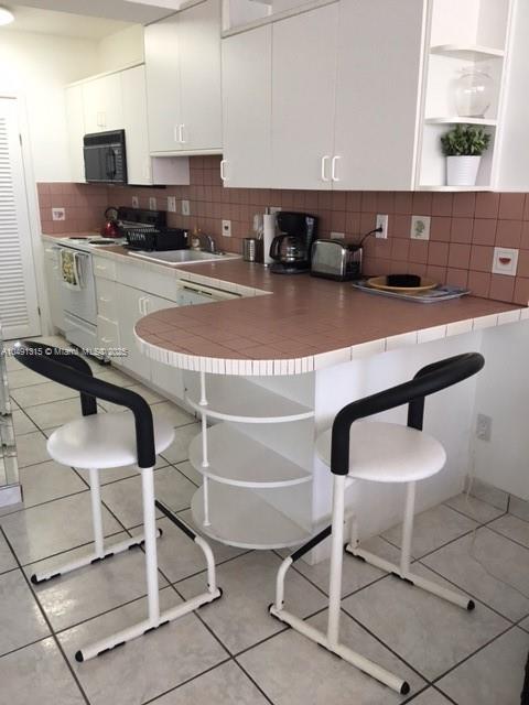 A kitchen features white cabinets, a tiled countertop breakfast bar, and two modern bar stools — 100 LINCOLN RD # 1236, Miami Beach FL 33139, MIAMI BEACH, FL