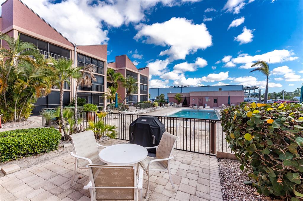 A patio with a table and chairs overlooks a swimming pool and apartment building — 3170 MATECUMBE KEY ROAD UNIT 115, PUNTA GORDA, FL