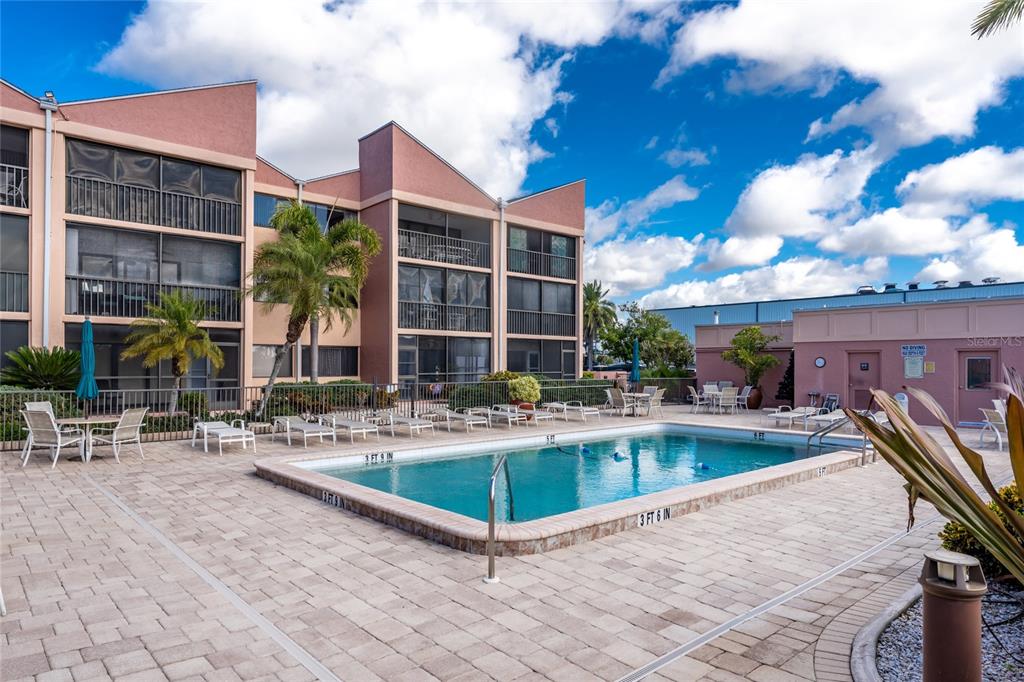 A swimming pool sits on a paved patio in front of a multi-story apartment building — 3170 MATECUMBE KEY ROAD UNIT 115, PUNTA GORDA, FL
