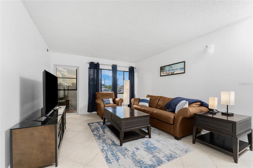A living room features a brown leather sofa, matching armchair, coffee table, and tile flooring — 3170 MATECUMBE KEY ROAD UNIT 115, PUNTA GORDA, FL