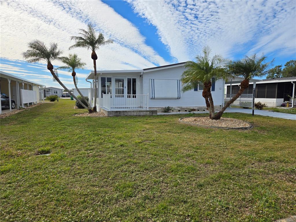 A single-story mobile home with a white exterior, a front porch, and several palm trees — 8479 TANAKA DRIVE, ENGLEWOOD, FL