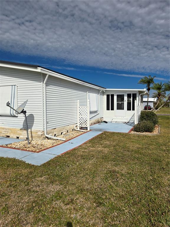 A light-colored mobile home with a satellite dish, stone skirting, and a blue concrete walkway — 8479 TANAKA DRIVE, ENGLEWOOD, FL