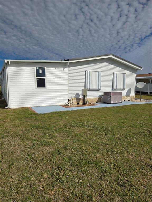 The exterior of a light-colored mobile home features a central air conditioning unit and windows — 8479 TANAKA DRIVE, ENGLEWOOD, FL
