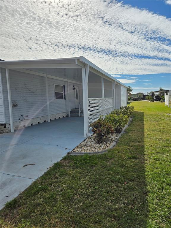 A mobile home exterior features a covered carport, a screened porch, and a landscaped garden bed — 8479 TANAKA DRIVE, ENGLEWOOD, FL