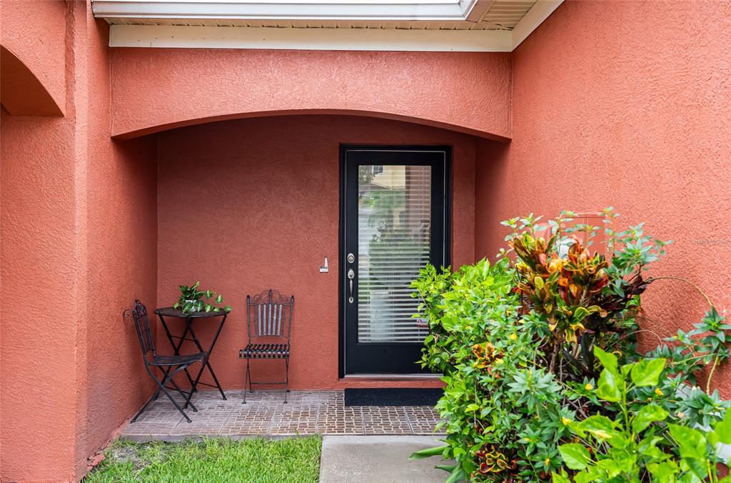 A terracotta-colored home exterior features a black front door, a small bistro set, and landscaping — 11014 BLAINE TOP PLACE, TAMPA, FL